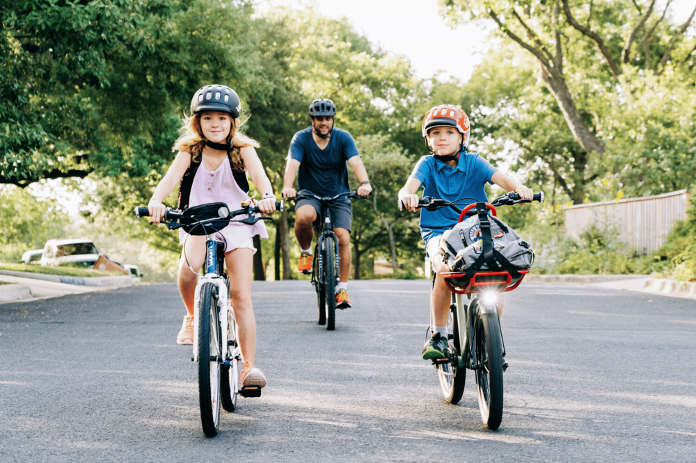 Ein Mädchen, ein Junge und im Hintergrund ein Erwachsener radeln auf woom Bikes