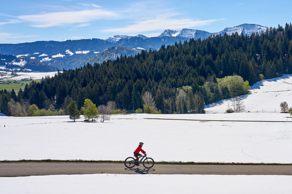 Fahrradfahrerin fährt auf der Straße, im Hintergrund ist eine winterliche Berglandschaft