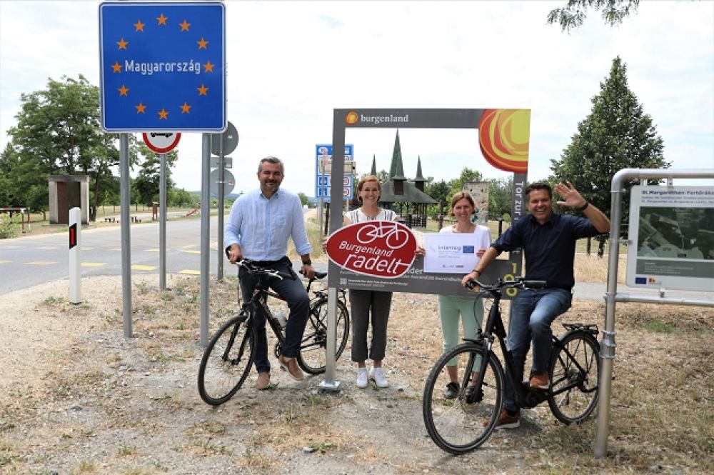 4 Radfahrer mit ihren Fahrrädern posieren am ungarischen Grenzschild